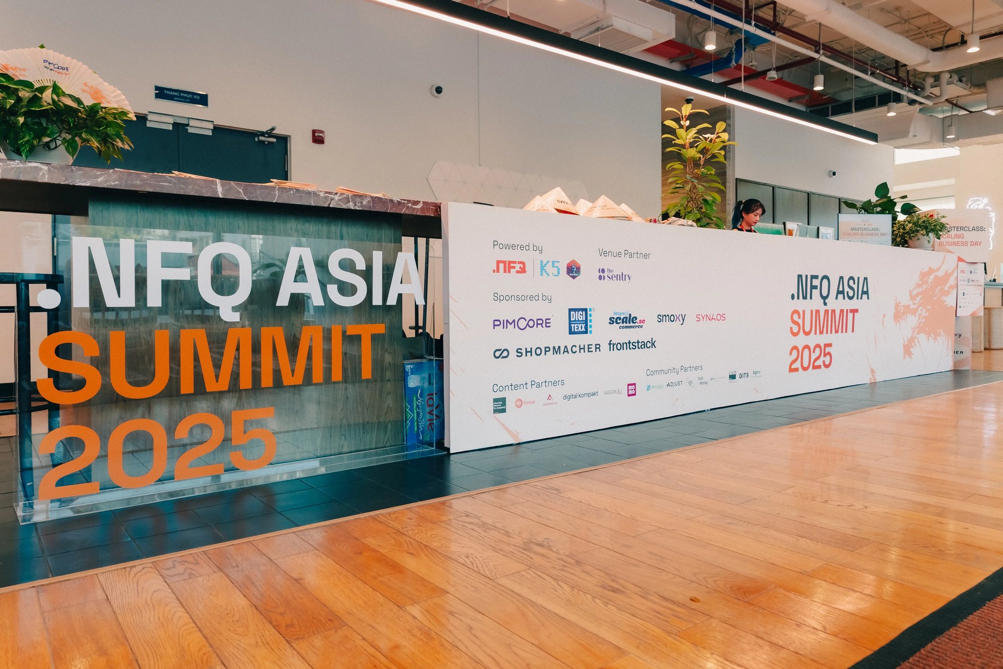 Panel showing an event check-in held in a bright open space . Many sponsors are portrayed at the entrance.