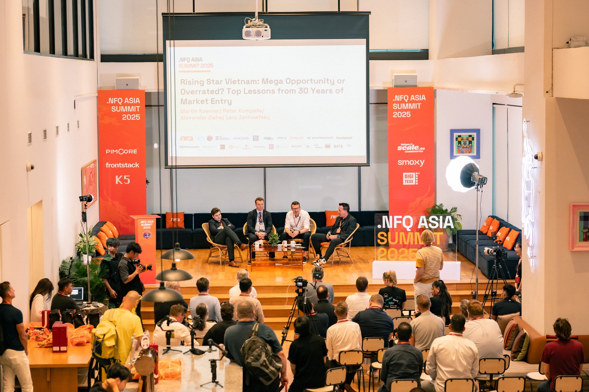 Participants attending a conference held by 4 presenters on a branded stage in a bright conference room.