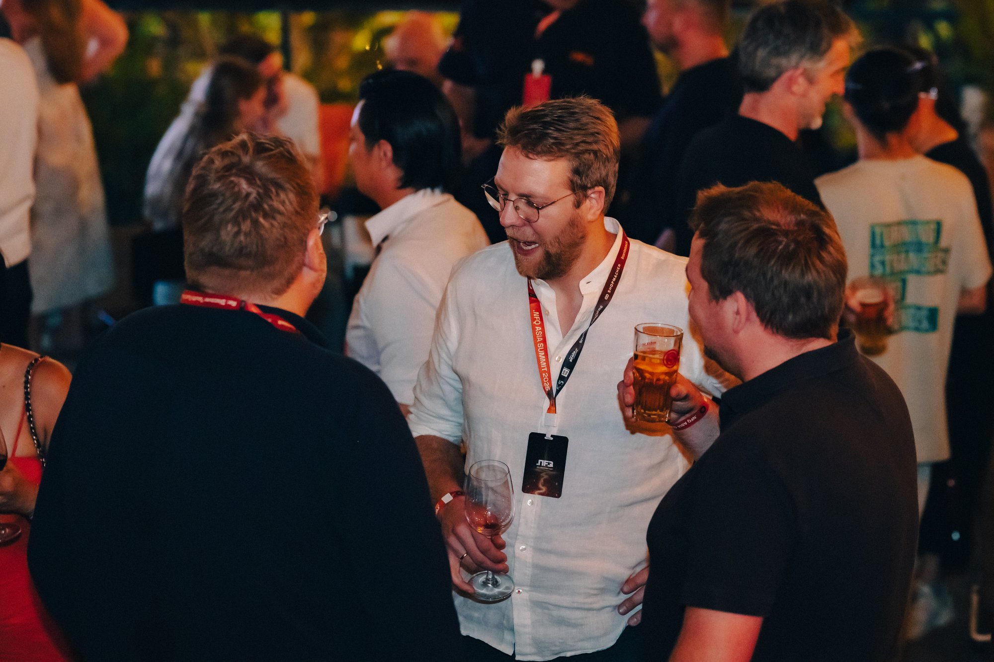 Three business event attendees talking in a round at a late occurring event with a drink in their hand.